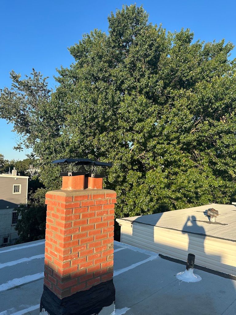 Brick chimney with a black metal chimney cap rising from a flat roof