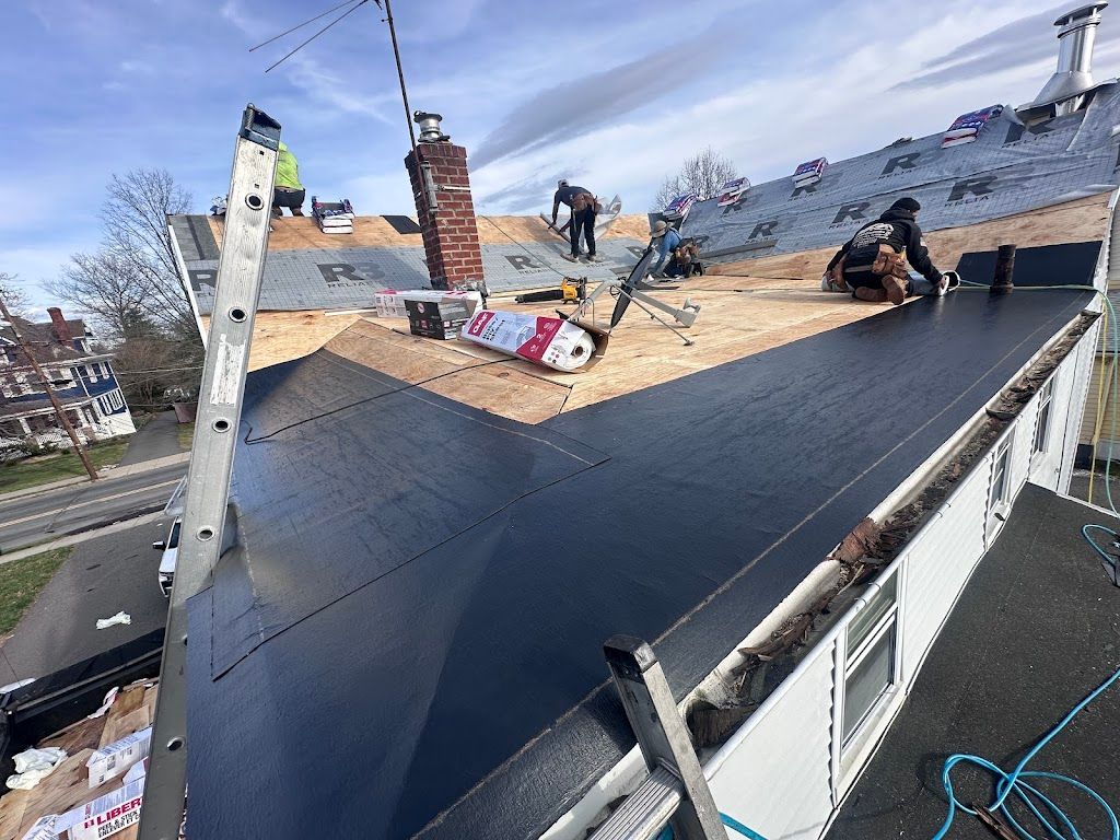Crew installing a new flat roof membrane next to a sloped roof section